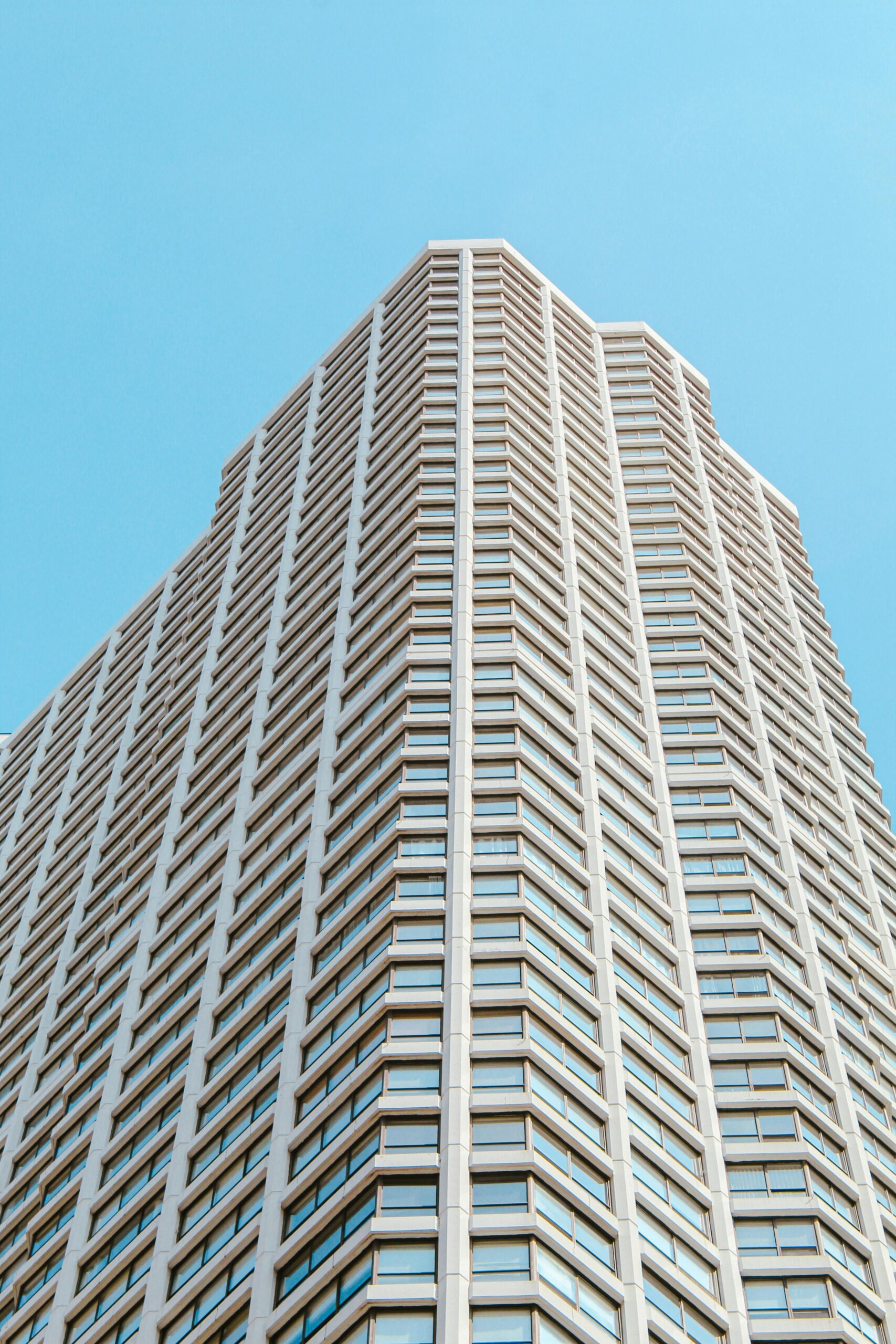 Upward view of a modern skyscraper set against a clear blue sky.